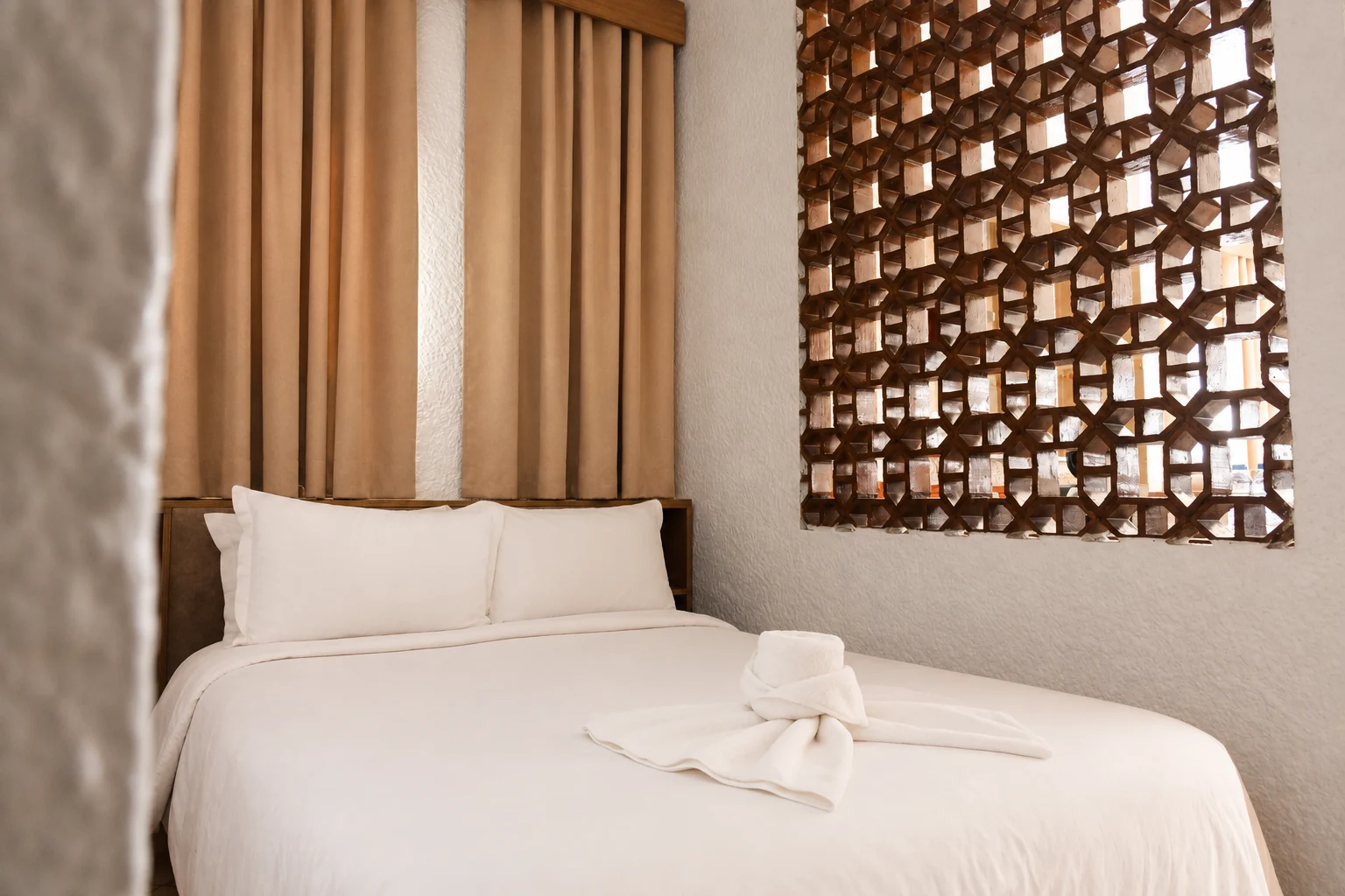 Lit double, rideaux et claustra en bois dans une chambre du Studiotel Afoud